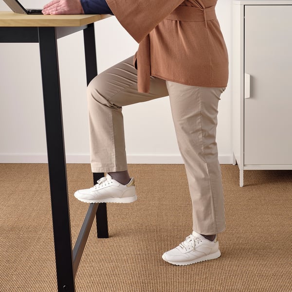 Person standing at high table with footrest for support.