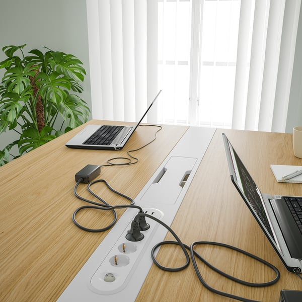 Office table with laptops and power strips, featuring cable management and a plant.
