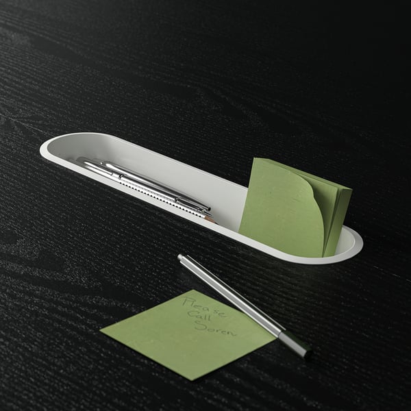 A minimalist tray holds pens and green sticky notes on a dark table.