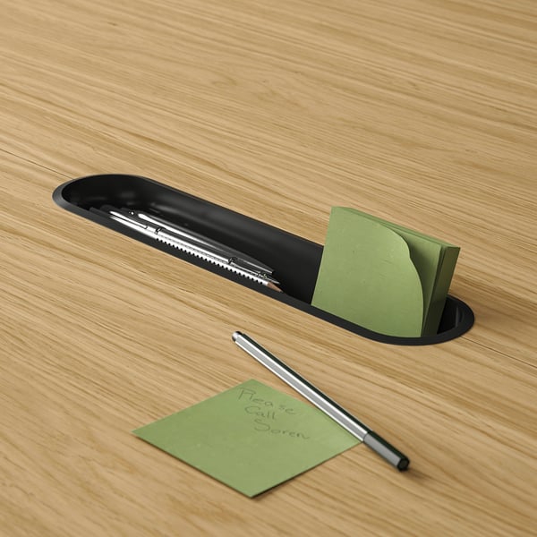 Black table slot with pen tray and notepad holder. Green sticky notes and pen nearby.