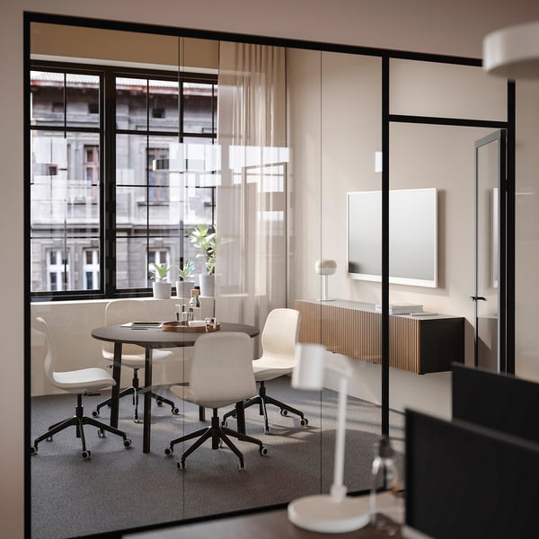 Small modern office with round table & four chairs, facing large windows, suitable for small group discussions.