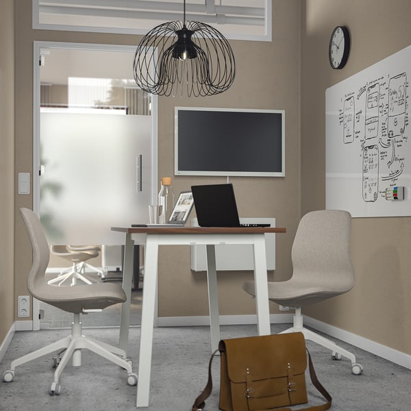 Small modern office with MITTZON white table, two chairs, laptop, monitor, and brown bag; grey walls and glass door.