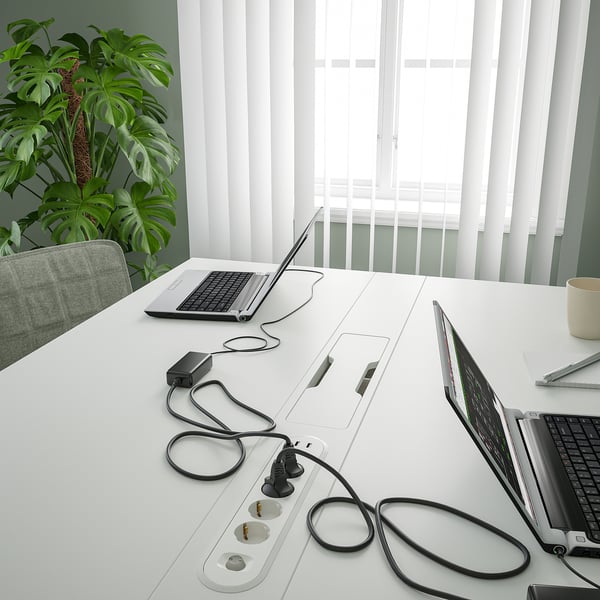 Conference table with laptops and power strips, featuring cable management.