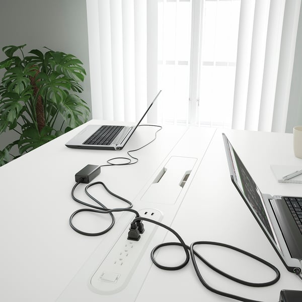 Modern office conference table with laptop chargers and cable management, suitable for sitting and standing.