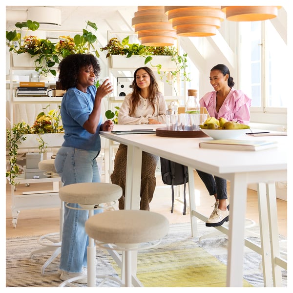 Three people collaborate at a modern MITTZON table with cable management in a bright, plant-filled room.