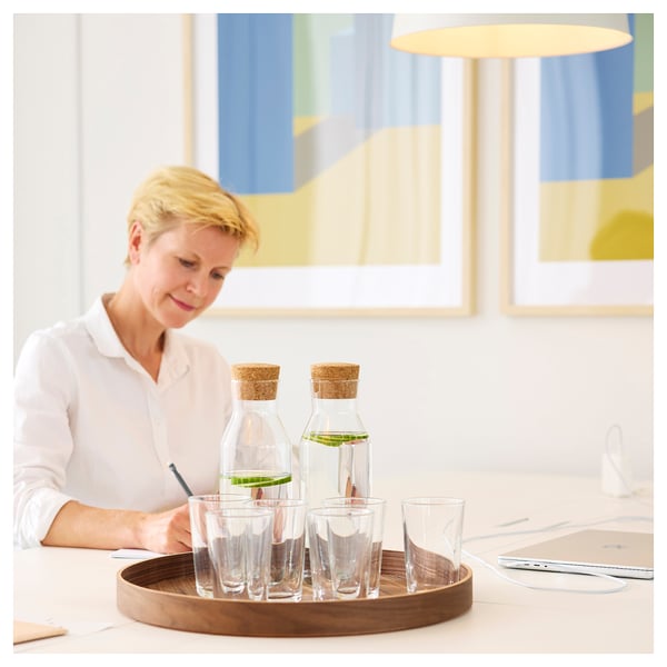 Person at table with water bottles, glasses, laptop, and papers.