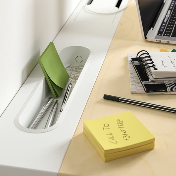 Desk tray with pens, sticky notes, notebook, and laptop for productivity.