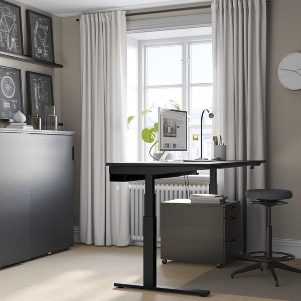 Modern home office with black MITTZON desk, grey storage, white curtains. Minimalist corner workstation with large window.