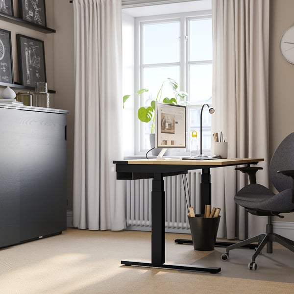 Modern home office with MITTZON desk, tall grey cabinet, black chair. Desk has dual motors, hardwood top. Large window, bright decor.