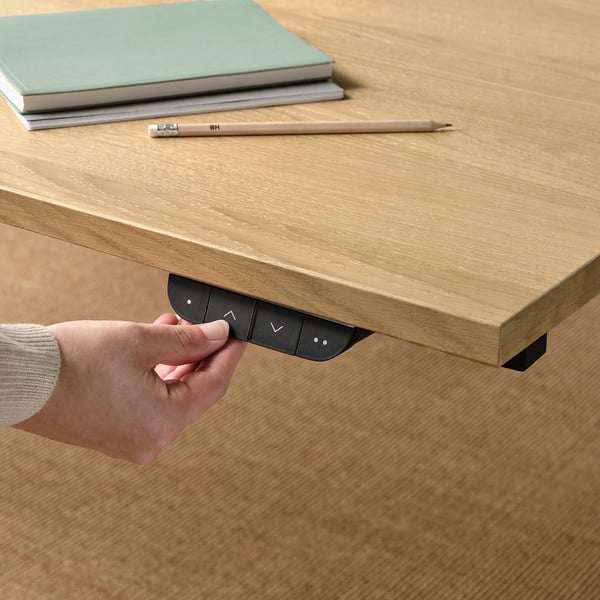 A hand adjusting a control panel on the side of an electric sit-stand desk, demonstrating its height adjustment feature.