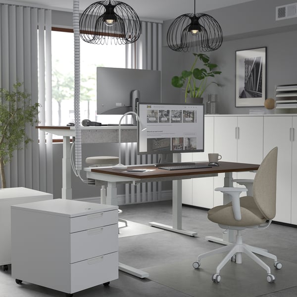 Modern home office: white MITTZON sit/stand desk, chair, and decor. Tall, adjustable, with dual monitors. Grey walls, larger than typical desks.
