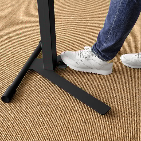 Person using black height-adjustable laptop table, wearing jeans and trainers.
