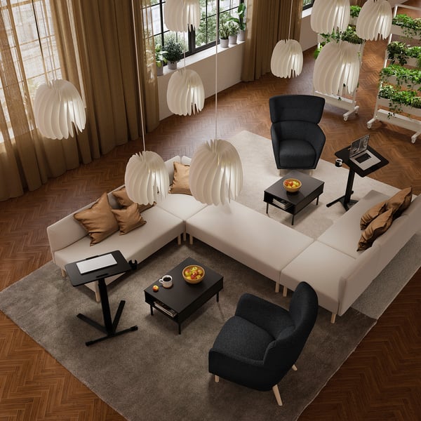 Modern living room with wooden floors, sectional couch, desks, armchair, and lamps. Rug and plants by windows.
