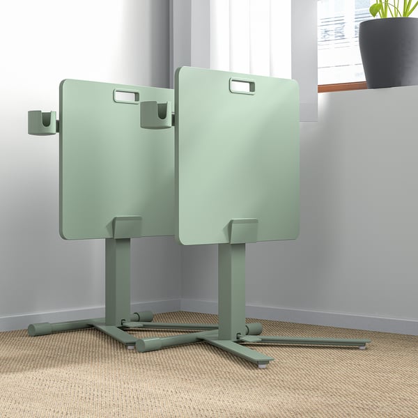 Two green height-adjustable laptop tables with handles and castors in an office setting.