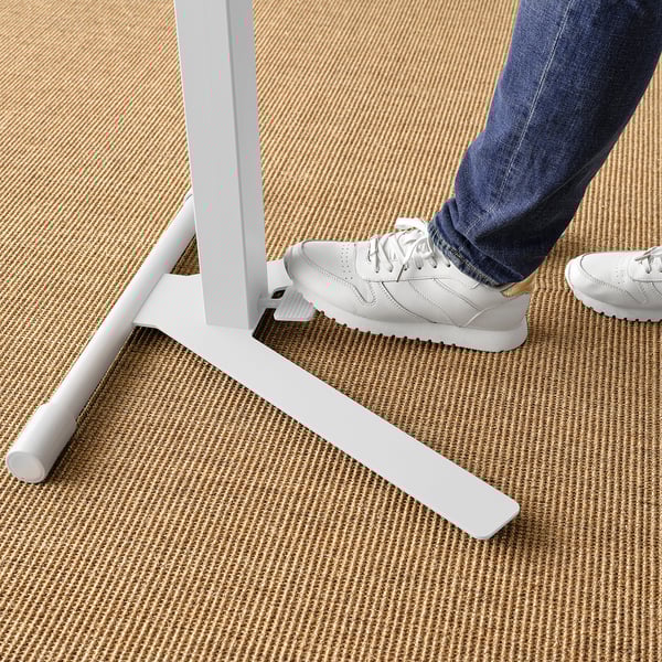Person using MITTZON laptop stand; adjusts with foot, sturdy design on woven carpet.