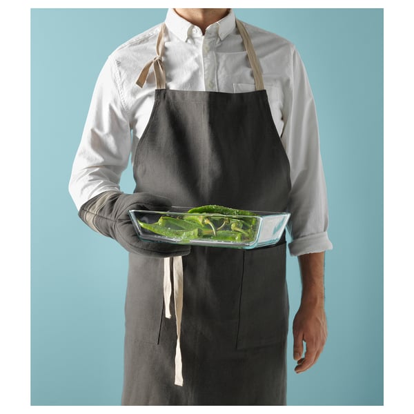 Person in white shirt and black apron holding clear glass tray with green vegetables.