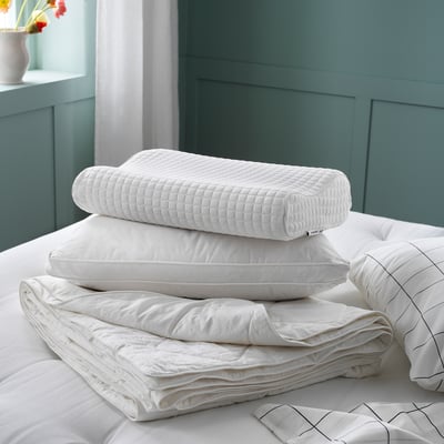 White bedding stack: MJUKDÅN silk-filled cotton duvet, pillow, and folded blanket on green wall.