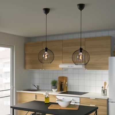 Modern kitchen with wooden cabinets, black countertop, pendant lights, cutting board, sink, stove, fridge, potted herb.
