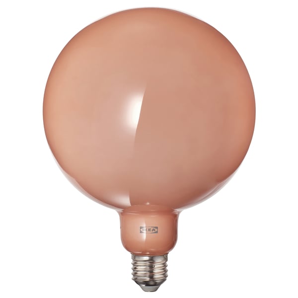 A rounded light bulb with peach-colored glass by IKEA, featuring a warm glow and elegant simplicity.