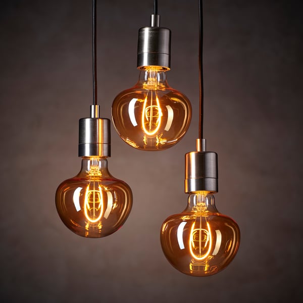 Three vintage-style light bulbs hang, emitting warm, amber glow; bell-shaped with exposed filaments.