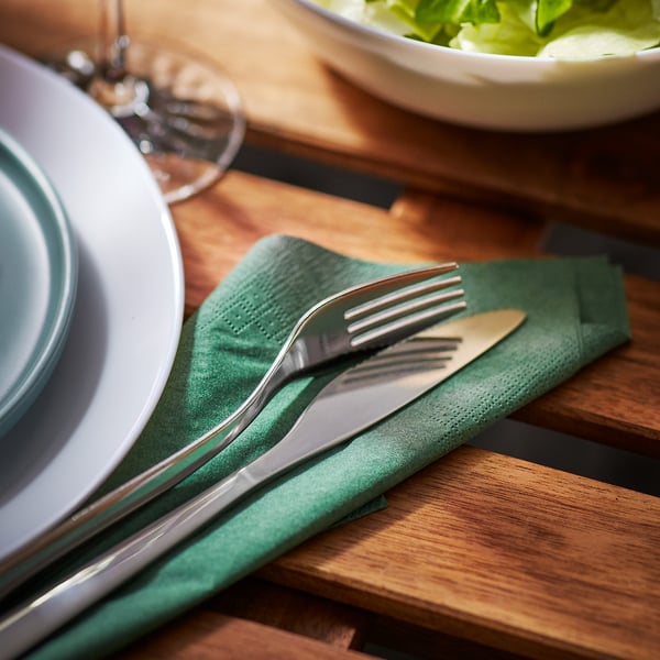 Wooden table set with green napkin and stainless steel fork and knife, ready for dining.