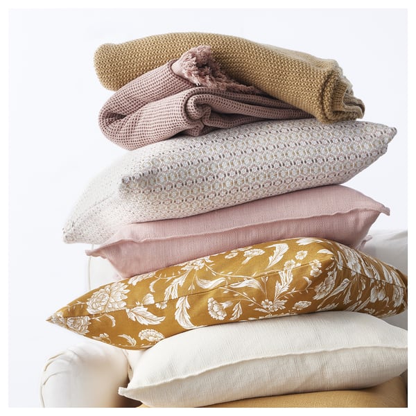 Stack of pillows in neutral colours, including yellow floral and plain white, stacked neatly against a white background.