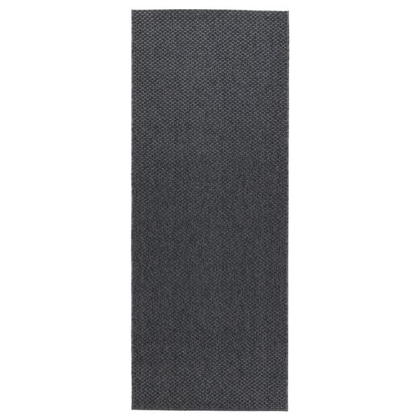 A rectangular MORUM rug in dark grey. Made of polypropylene, its designed for indoor and outdoor use, suitable for hallways and balconies.