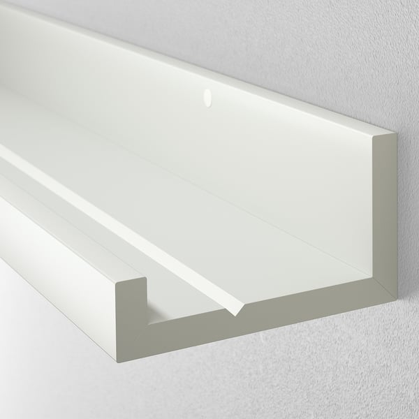 White wall shelf with a groove for holding frames. Mounted on a light-colored wall.