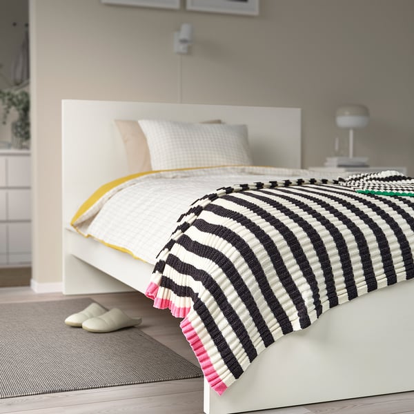 Cosy black & white striped MOSSMOTT throw on bed, larger than slippers, soft recycled polyester.