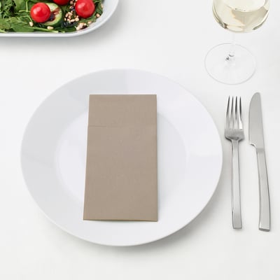 A place setting with a white plate, two metal utensils, a folded napkin, and a side salad with a wine glass.