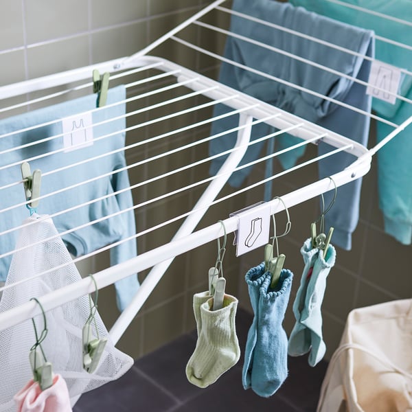 A folding drying rack with extended wings for hanging laundry. Socks and underwear hang from hooks.