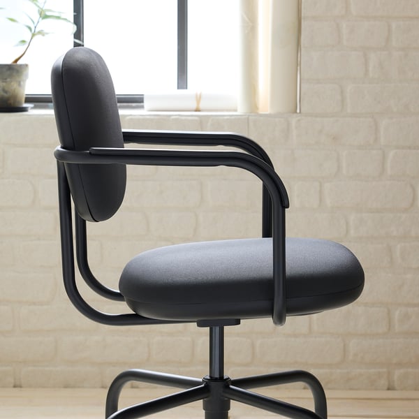 Black modern office chair with sleek design, padded seat and back, and adjustable height, set against a brick wall.