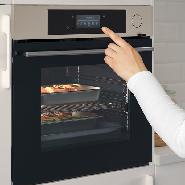Person using touch control on sleek, modern oven with digital display and racks inside.