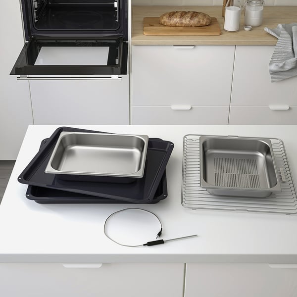Modern oven with open door, baking trays, and temperature probe on kitchen counter.