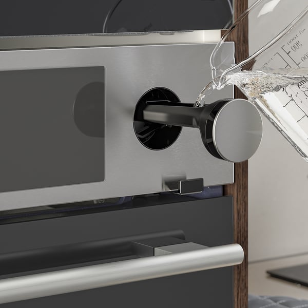 Water is being poured into a sleek, modern oven with a digital display and silver handle.