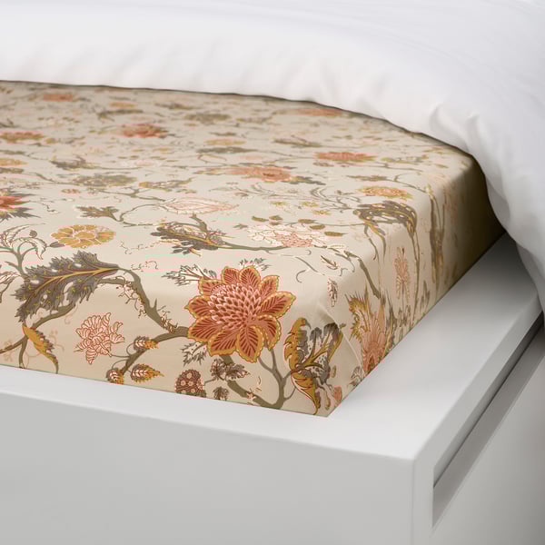 A bed with a beige floral-patterned fitted sheet, showcasing its elastic edge designed to fit mattresses up to 26 cm thick.