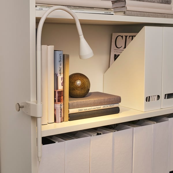 White clamp spotlight on shelf, illuminating books. Modern, adjustable design.