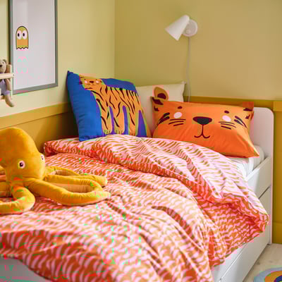 Bed with orange tiger-patterned duvet, two tiger pillows, and a yellow octopus toy. Bright, playful kids room decor.