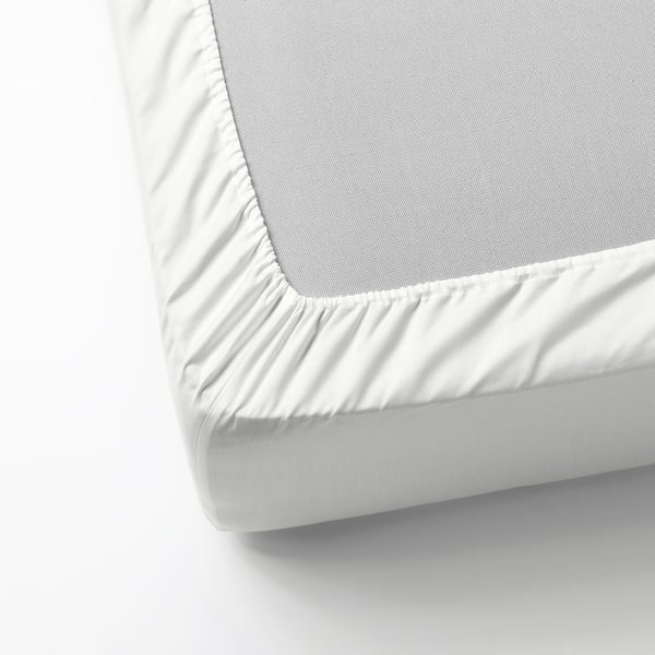 A neatly made bed with a white satin sheet, featuring a fitted sheet with elastic edging, designed for mattresses up to 26 cm thick.