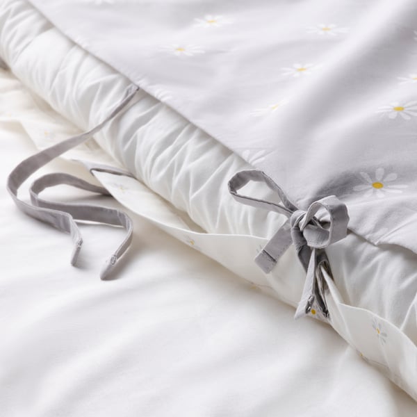 White duvet cover with grey daisies rolled, tied with ribbons, showcasing decorative close.