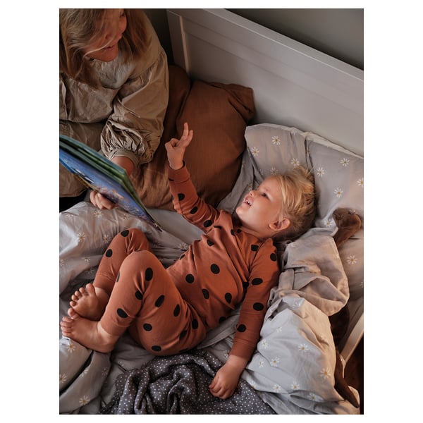 Child listening to bedtime story. Person in bed reading book. Soft daisy-patterned grey sheets.