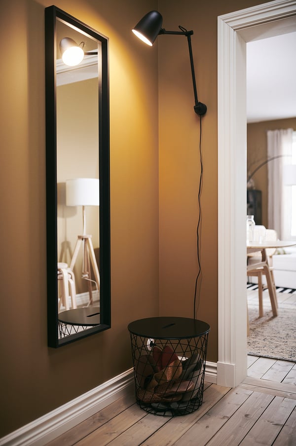 Image a black NISSEDAL mirror on wall, round wire basket below, and black wall lamp beside it.