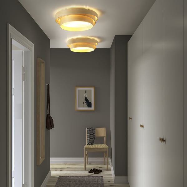 Stylish entryway with NÖSUND wood ceiling lamps, highlighting a chair, bag, pictures, and closets.