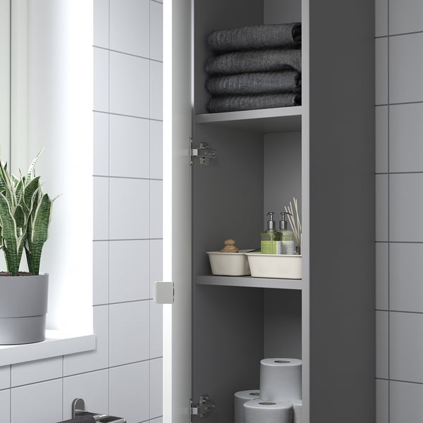 Bathroom cabinet with open door showing folded towels, toiletries, and toilet paper rolls on shelves.