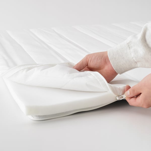 A hand opening a white, soft mattress pad with a zip, showcasing its removable cover.
