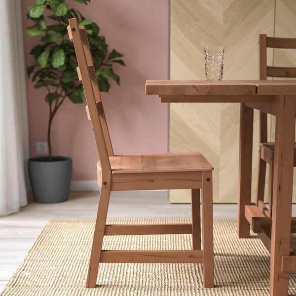 Angled seat wooden chair, high back, even weight distribution. At table, plant nearby.