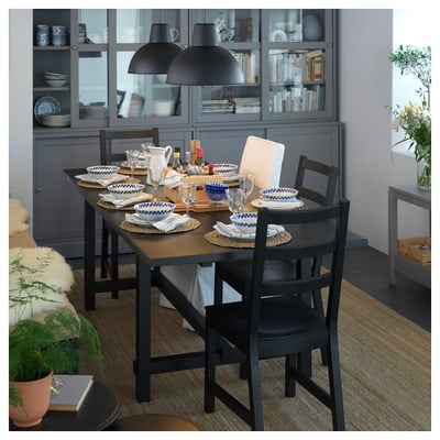 Stylish dining area with black NORDVIKEN chairs and table, grey cabinet, blue and white place settings, and hanging lamps.