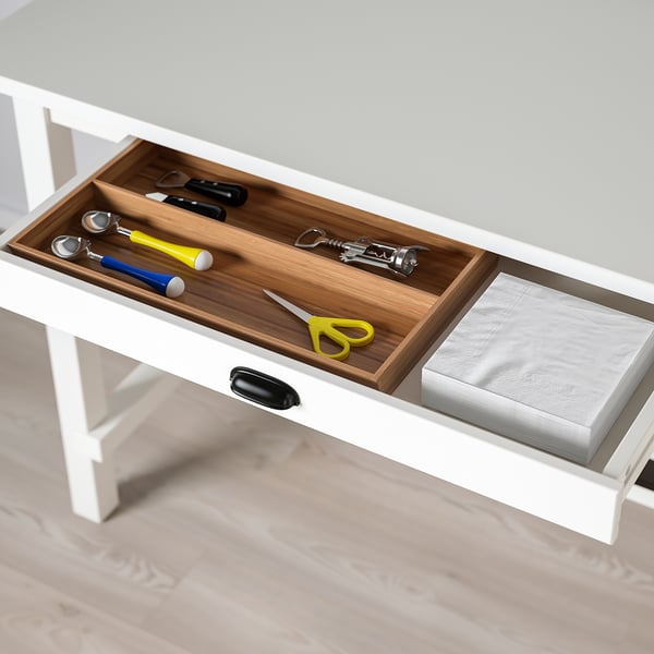 Open white drawer with wooden divider, holding kitchen utensils and a stack of napkins.