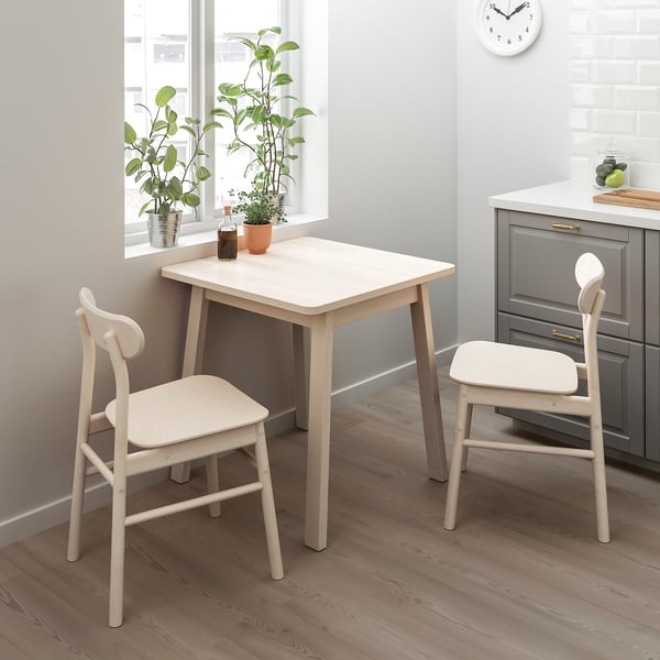 Minimalist scandinavian dining set with table and 2 chairs near window, rounded corners, 2 plants on sill.