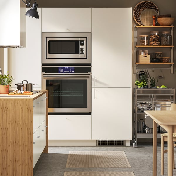 Modern kitchen with double oven, microwave, stainless steel appliances, light wood cabinets, and open shelving. Dining table on the right.